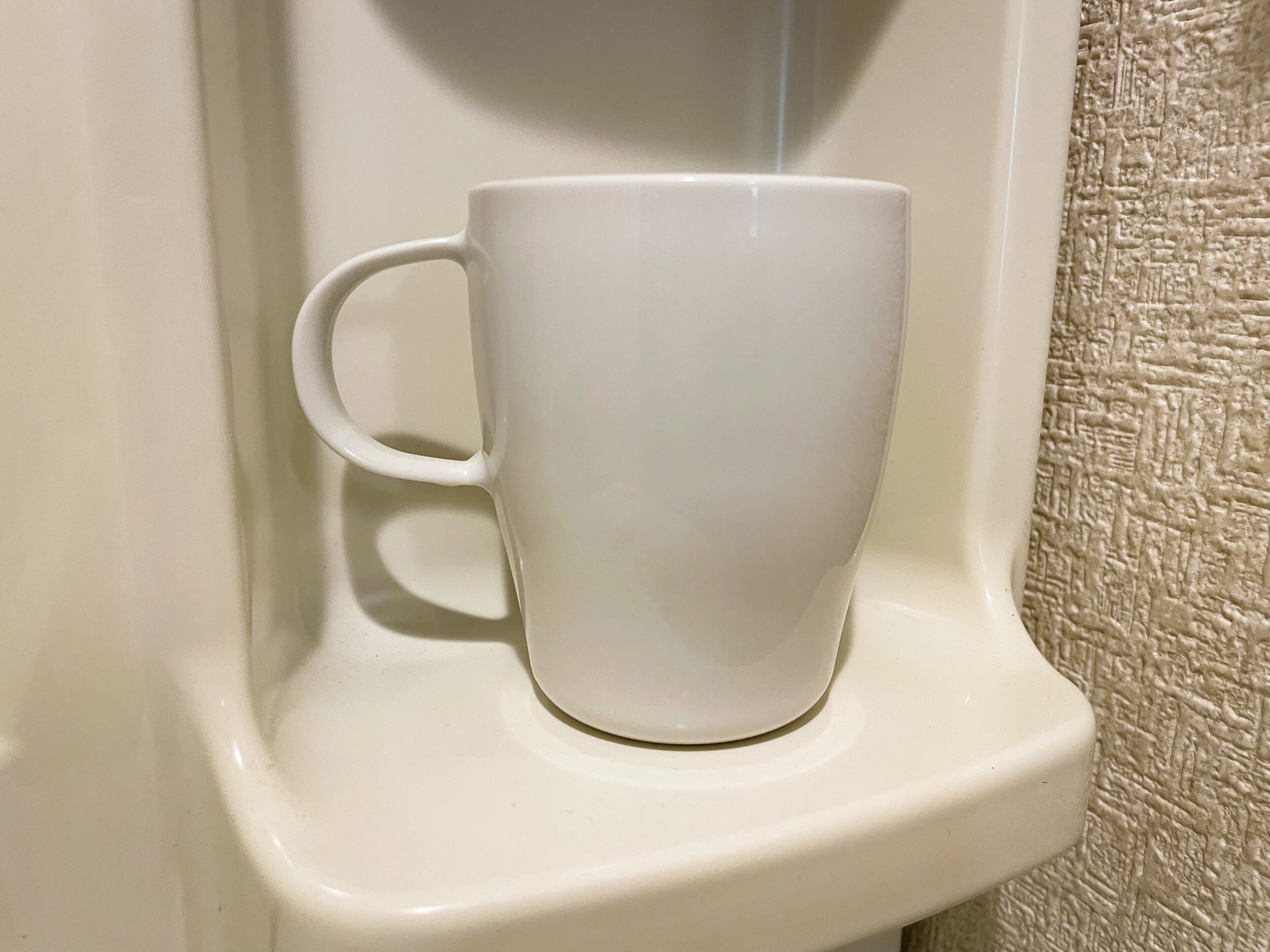 Una taza de cerámica blanca sobre una estantería blanca.