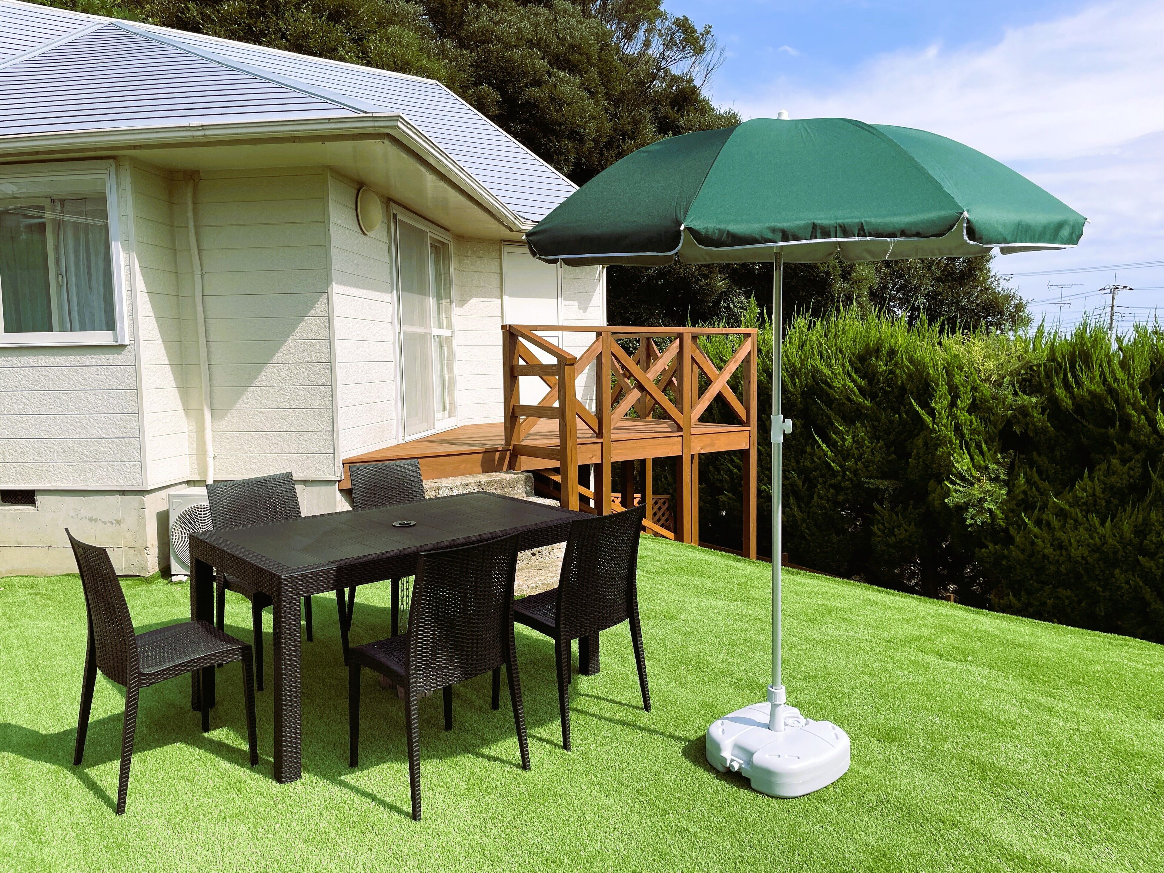 Una terrazza esterna con tavolo e sedie, un ombrellone verde e un molo di legno.