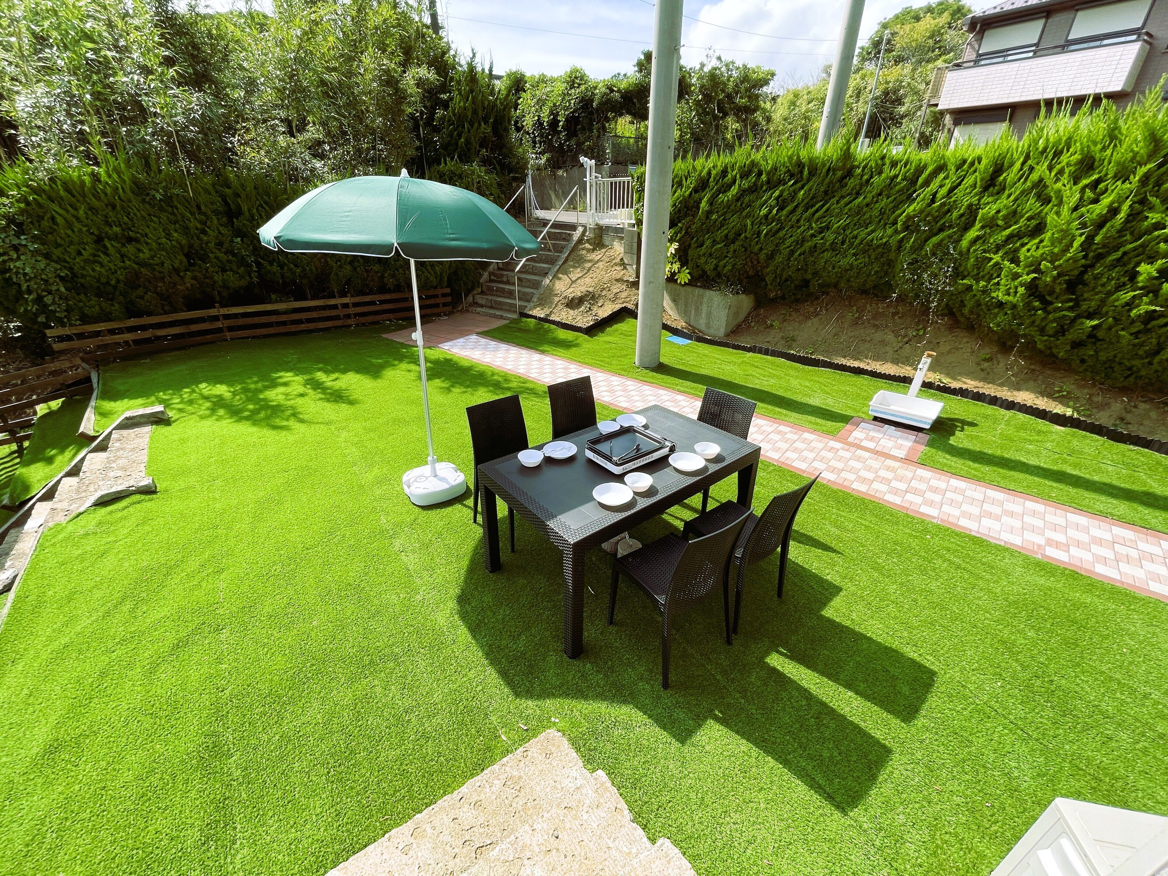 Un patio con una mesa dispuesta para cuatro personas, rodeada de sillas y un parasol verde.
