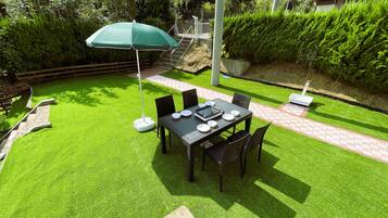 Un patio con una mesa dispuesta para cuatro personas, rodeada de sillas y un parasol verde.