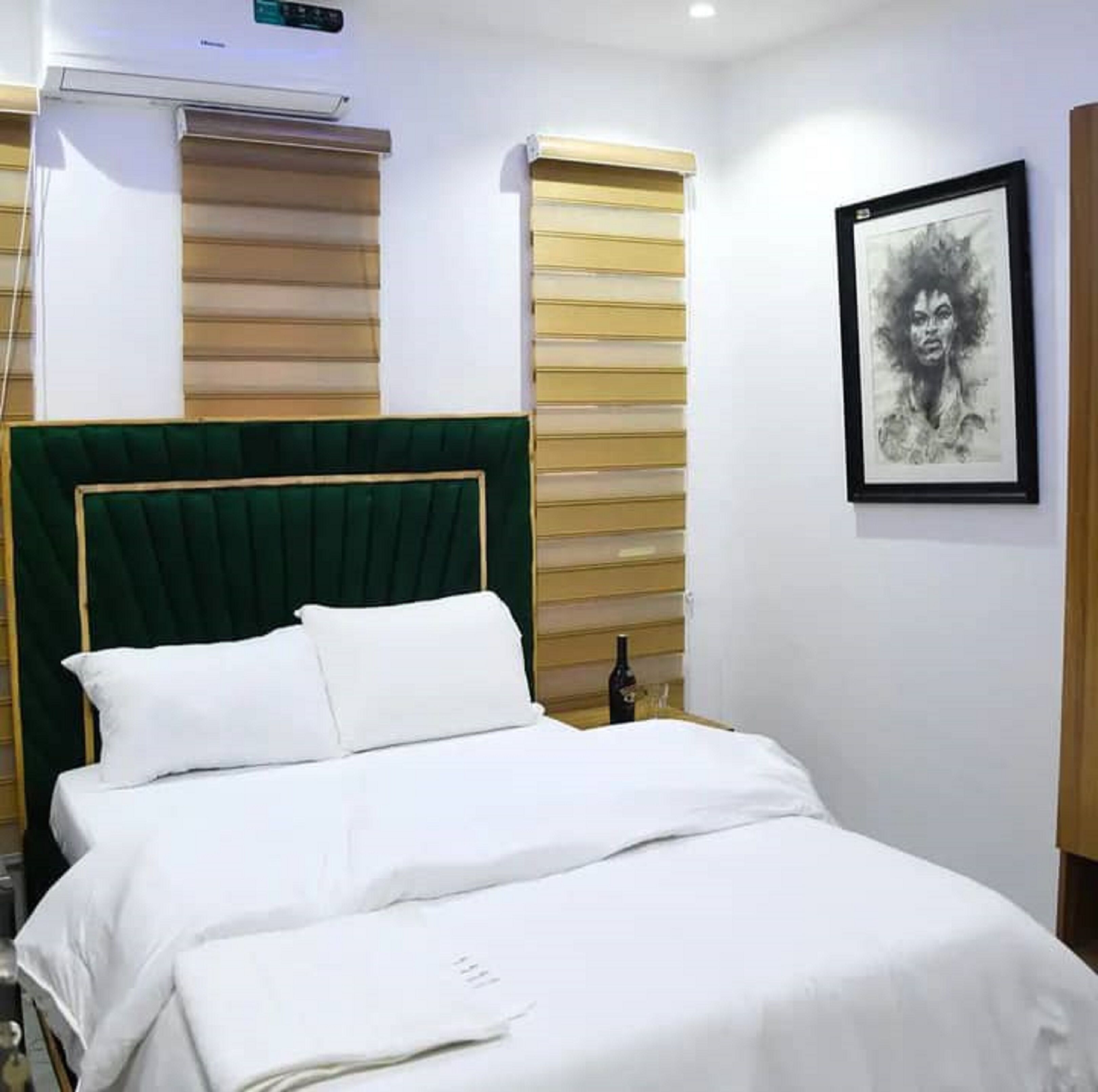 Een keurig opgemaakt bed met witte lakens, een met groen bekleden hoofdeinde, en een ingelijst kunstwerk aan de muur.