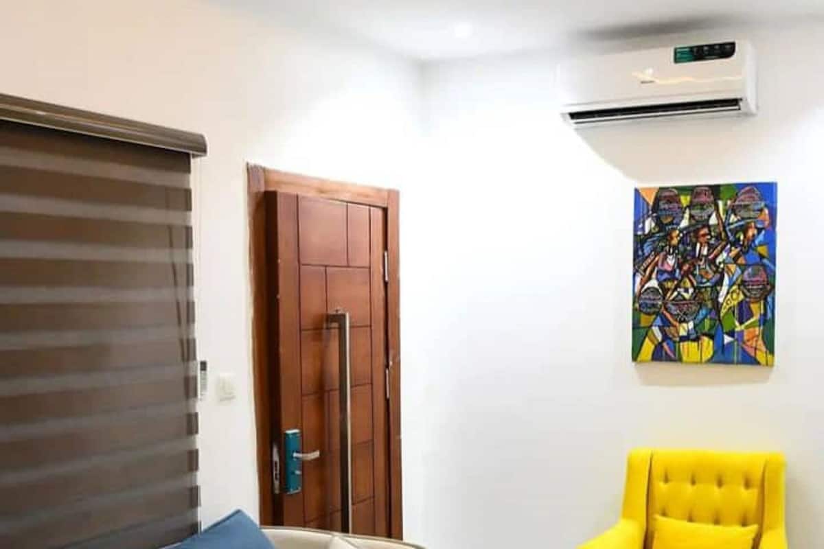Una sala de estar con un sofá, un sillón amarillo, una mesa roja y un aire acondicionado.