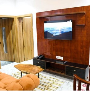 A modern living room with a wooden TV stand, a flat-screen TV, and a sofa. - Tito Empire (Lekki)