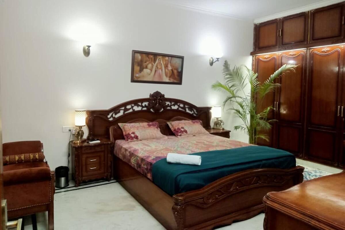 A bedroom with a wooden bed, nightstands, a chair, a wardrobe, and a painting on the wall.