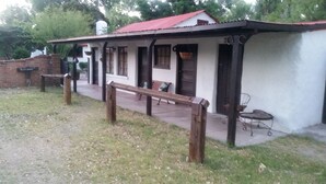 Un bâtiment rustique avec un toit rouge, un banc devant et un petit espace extérieur aménagé pour s’asseoir.