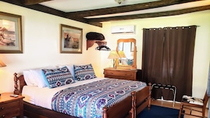 Une chambre à coucher avec un lit en bois, une table de chevet, une commode, un miroir, une lampe, une fenêtre avec des rideaux et un ventilateur de plafond.