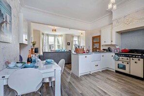 A modern kitchen with white cabinetry, a dining area with a white table and chairs, and a view of the living room.