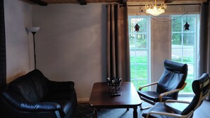 A room with a wooden ceiling, a black leather sofa, two leather chairs, a wooden table, and a chandelier.