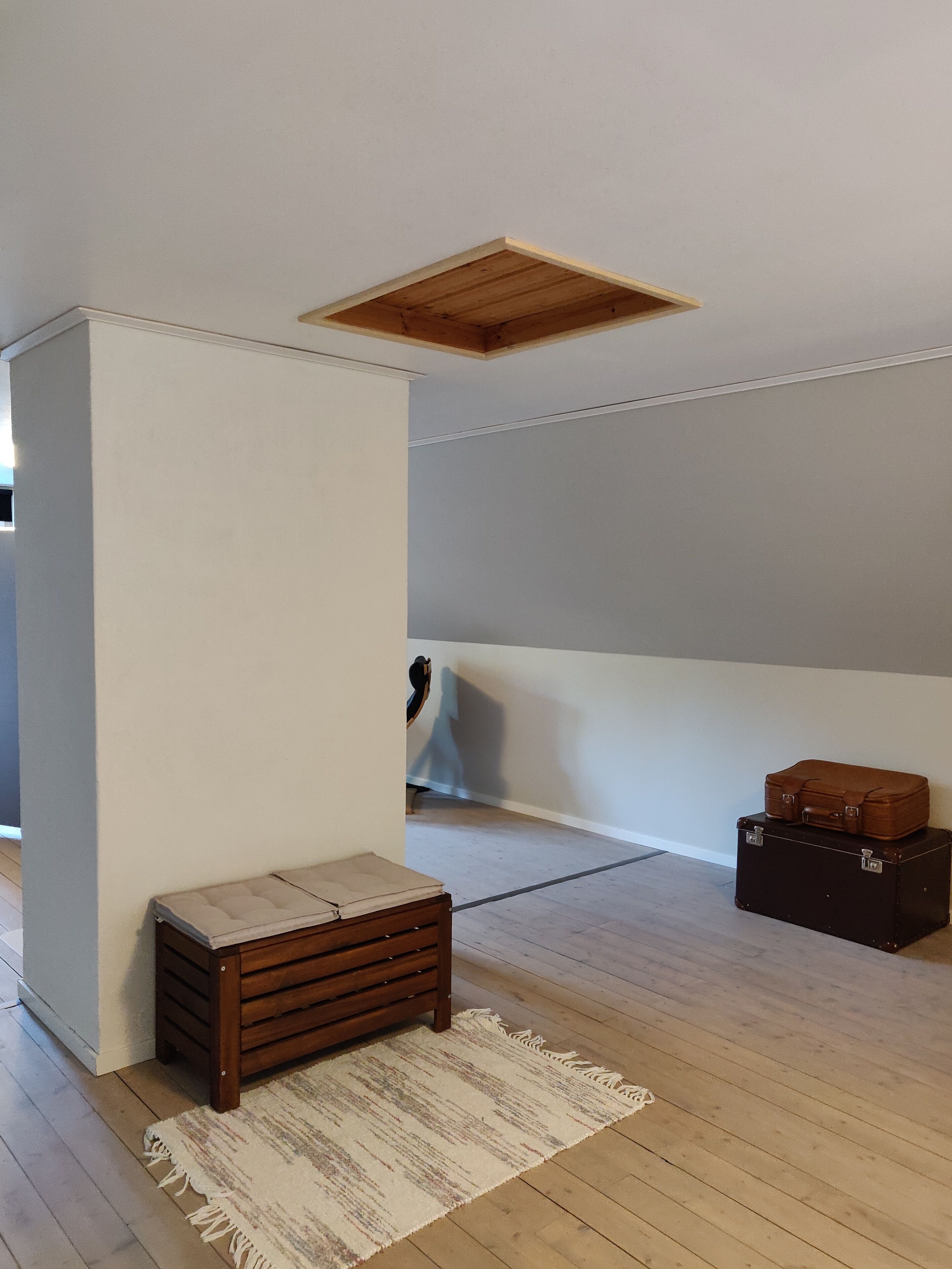 Una habitación con un banco de madera, un tapete y dos maletas apoyadas en la pared.