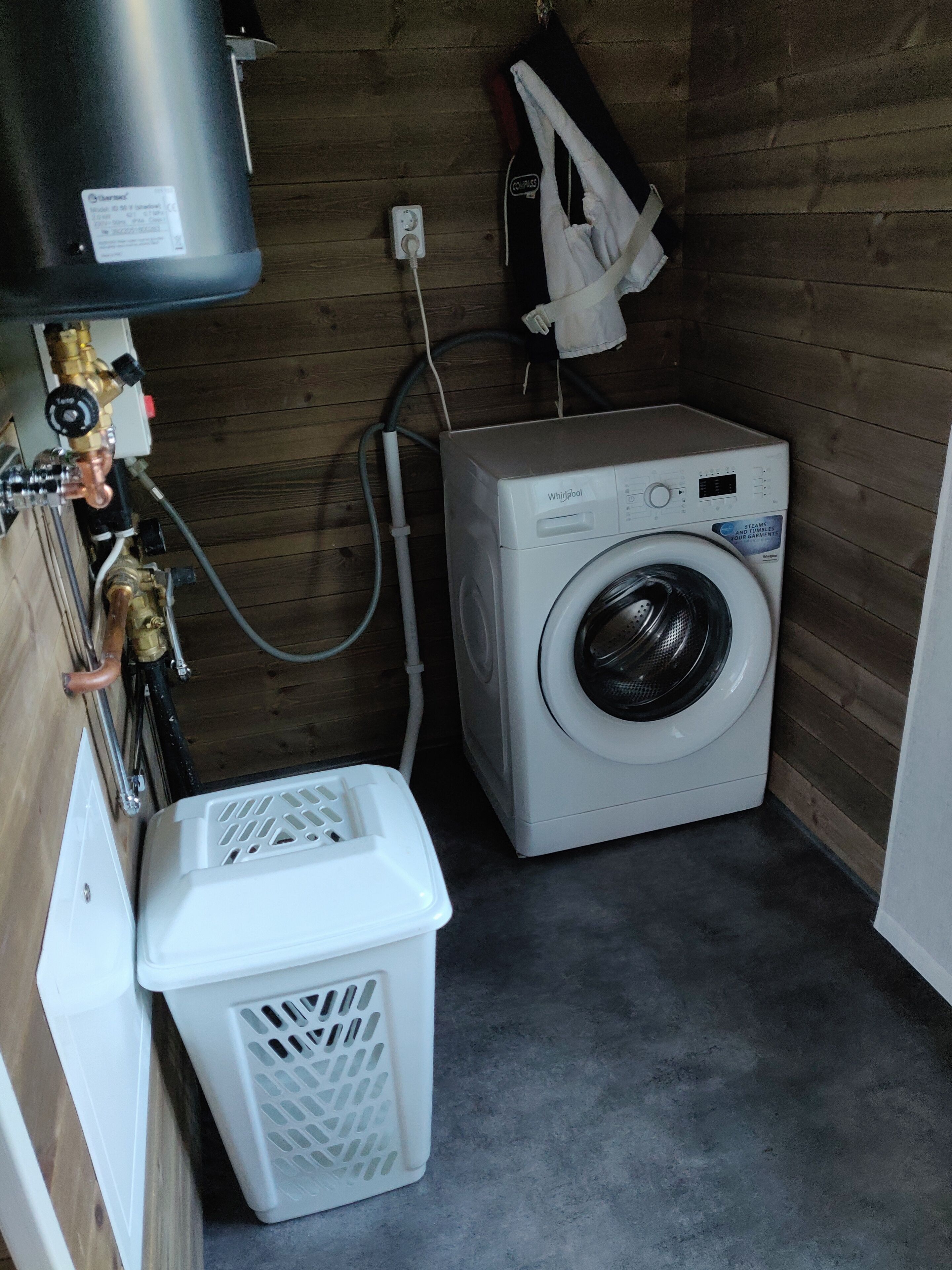 A compact laundry room with a washing machine, a dryer, a water heater, and a laundry basket.