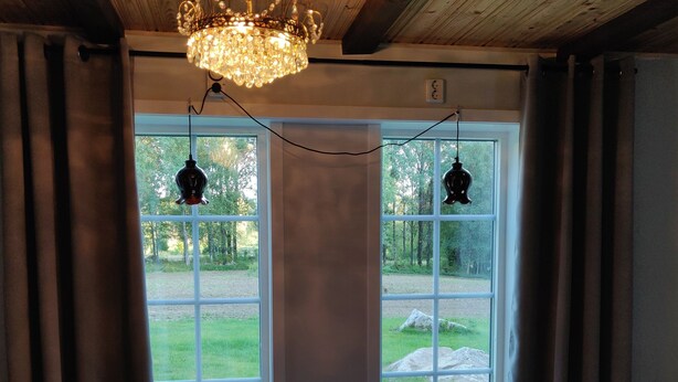 A room with a wooden ceiling, a chandelier, and large windows with curtains.
