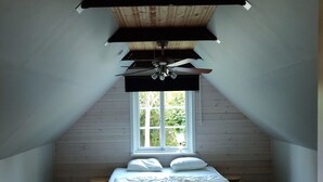 A bedroom with a sloped ceiling, a bed with pillows, a window, and a ceiling fan.
