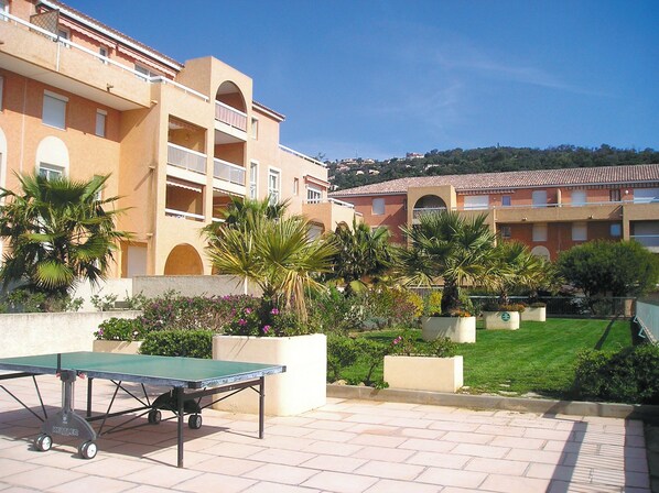 Un patio con mesa de ping pong, palmeras y un edificio con balcones.