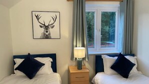 A bedroom with two beds, a nightstand, a lamp, and a window with curtains.