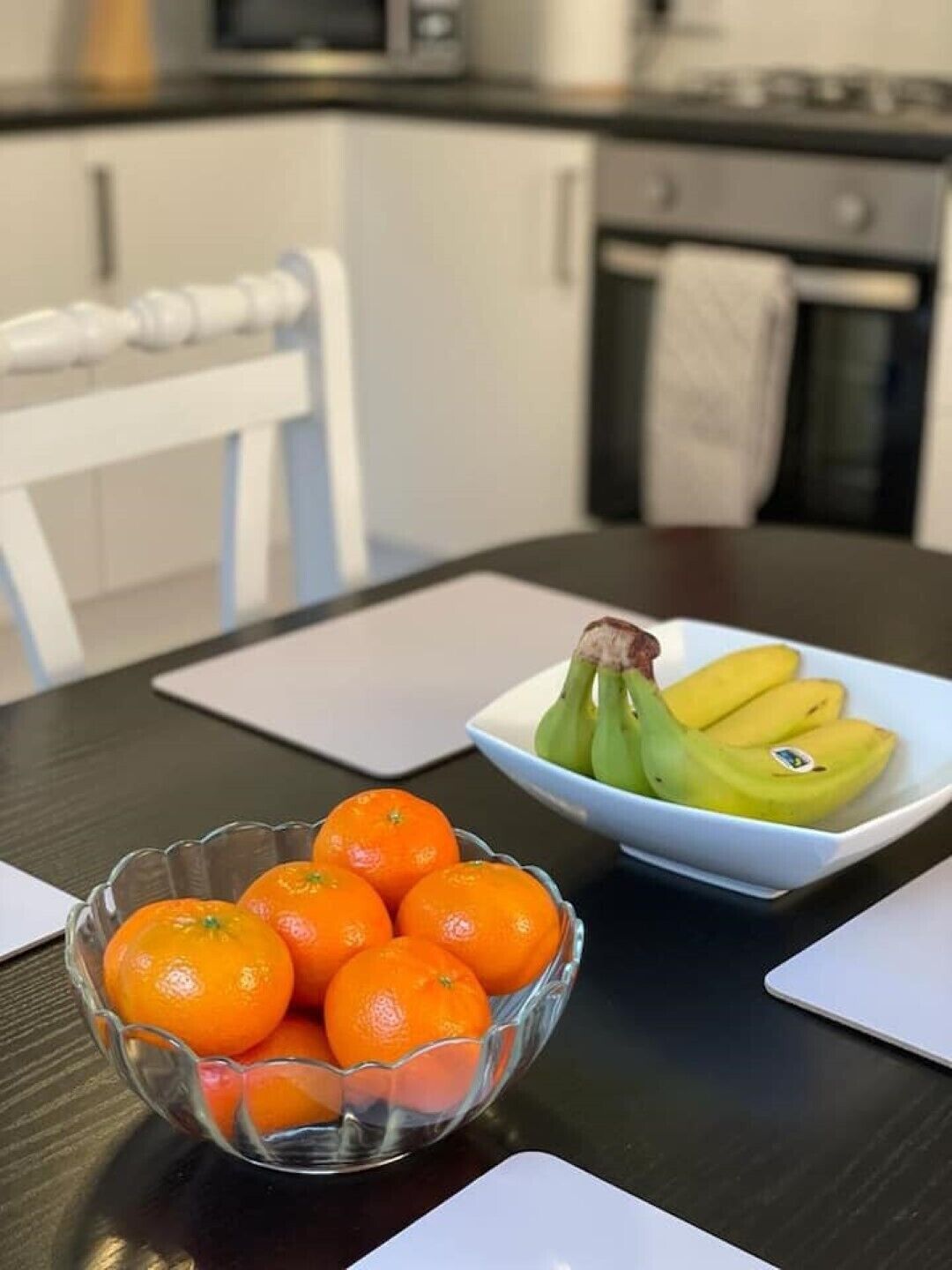 Une cuisine avec une table mise pour le repas, sur laquelle on aperçoit un bol d’oranges et une assiette de bananes.