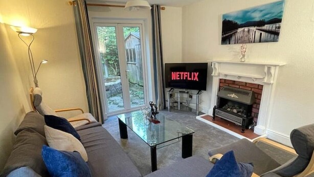 A living room with a sofa, a glass coffee table, a fireplace, and a TV displaying 'NETFLIX'.