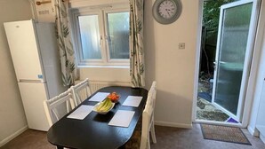 A dining area with a table, chairs, a clock, and a window with curtains.