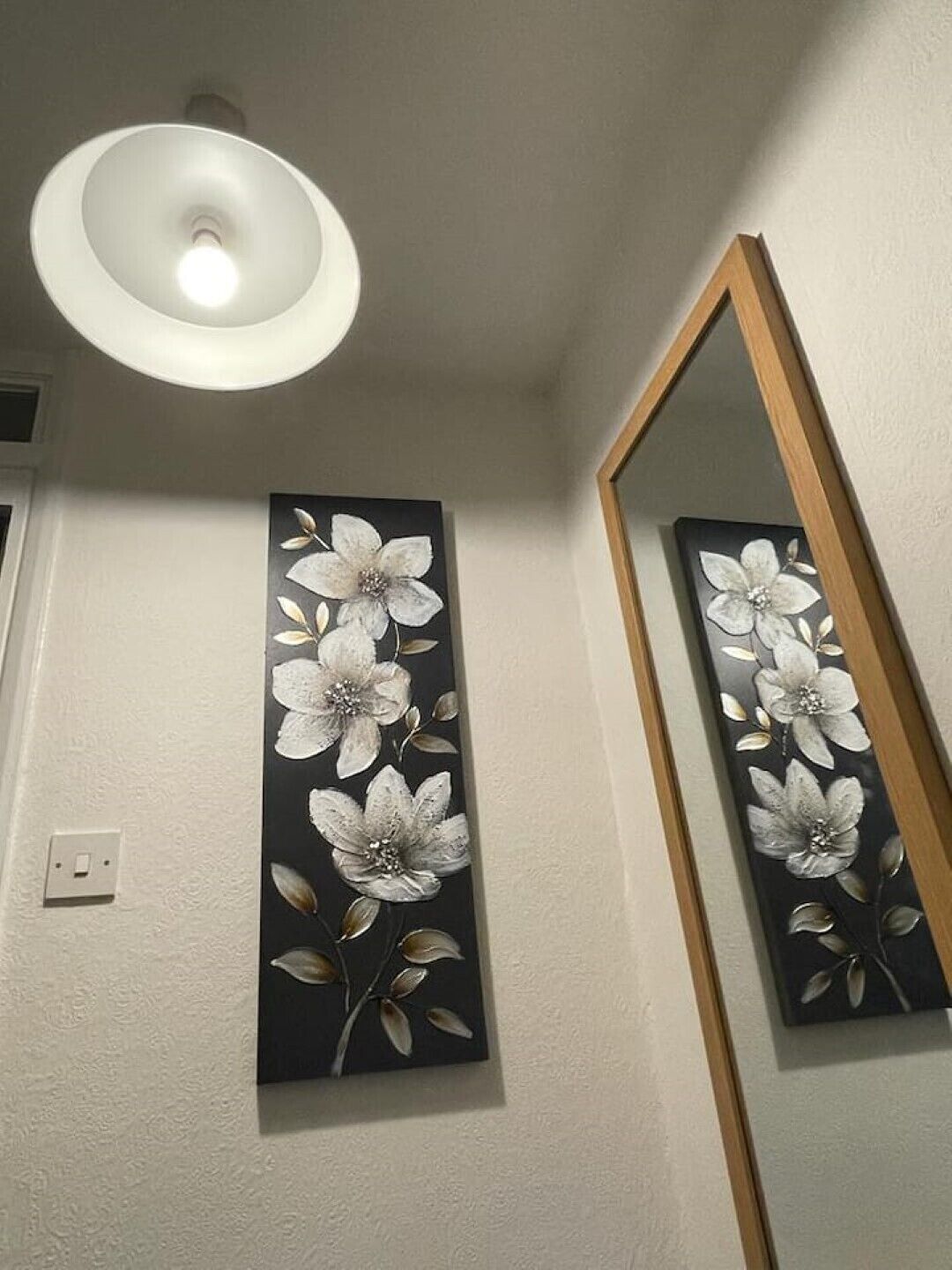 Et værelse med en loftlampe, et spejl på væggen og et blomsterbillede.