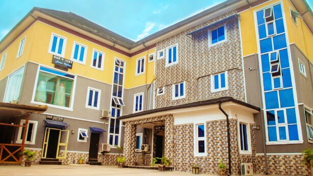 A multi-story hotel with a yellow facade, a central entrance, and a visible outdoor seating area. - Oak Valley Hotel & Event Center (Port Harcourt)