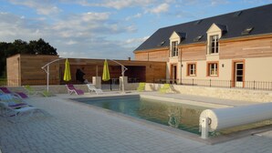 A swimming pool with lounge chairs and umbrellas, a covered seating area, and a building with a sloped roof. - Spacious house, private pool, 10 to 15 p. (Chémery)