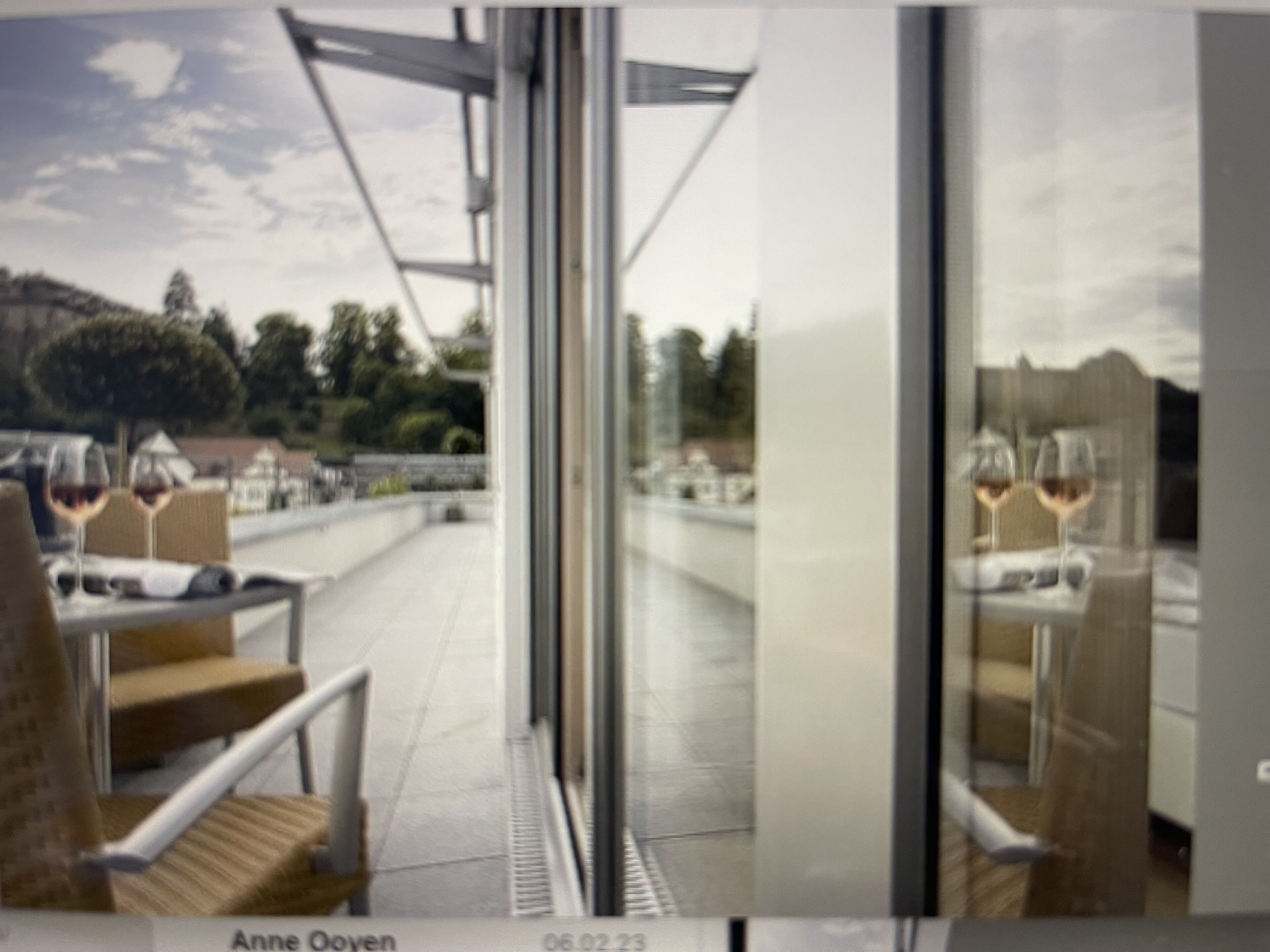 A restaurant with outdoor seating, a glass partition, and a view of the landscape.