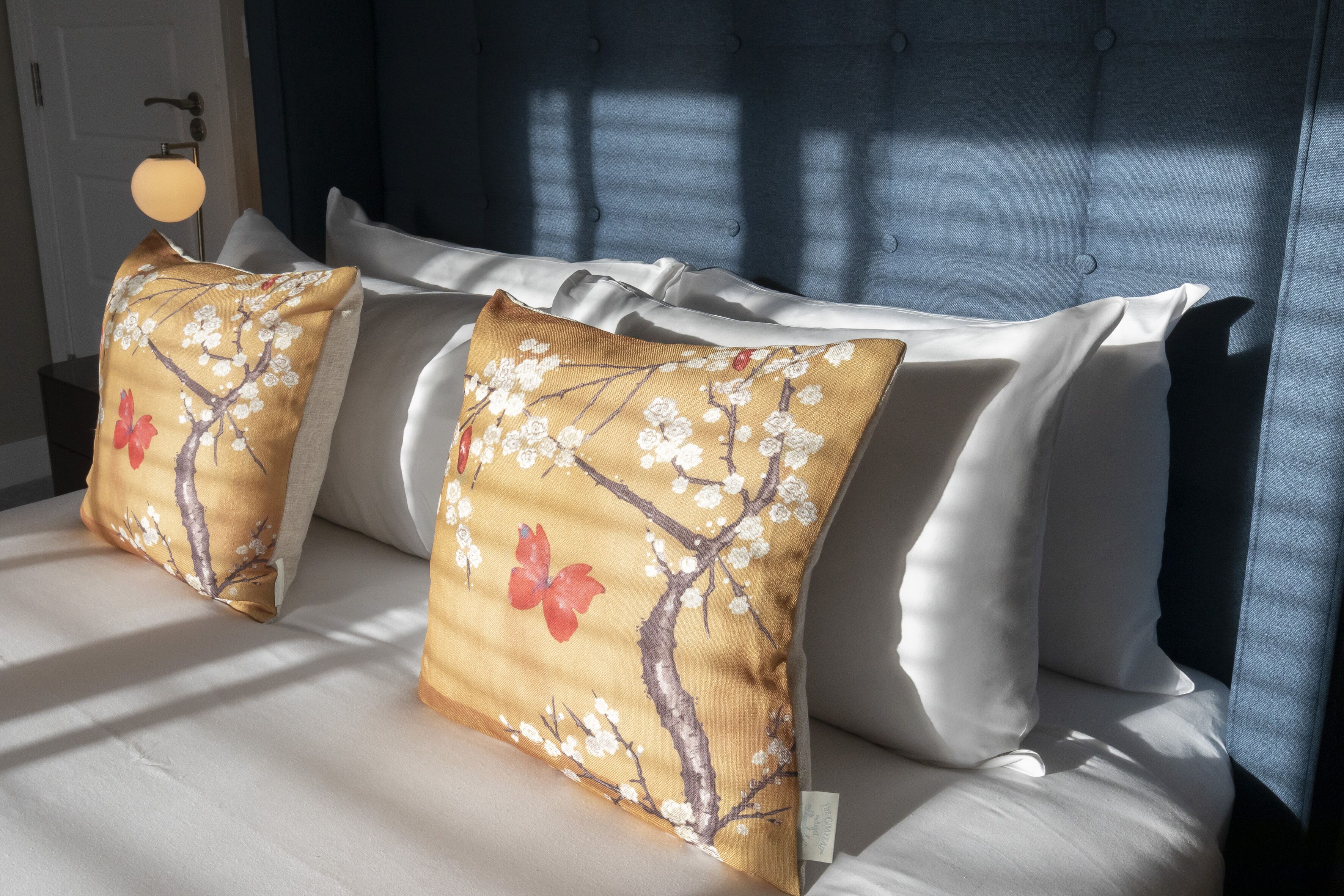 A bed with white linens and two decorative pillows with floral designs.