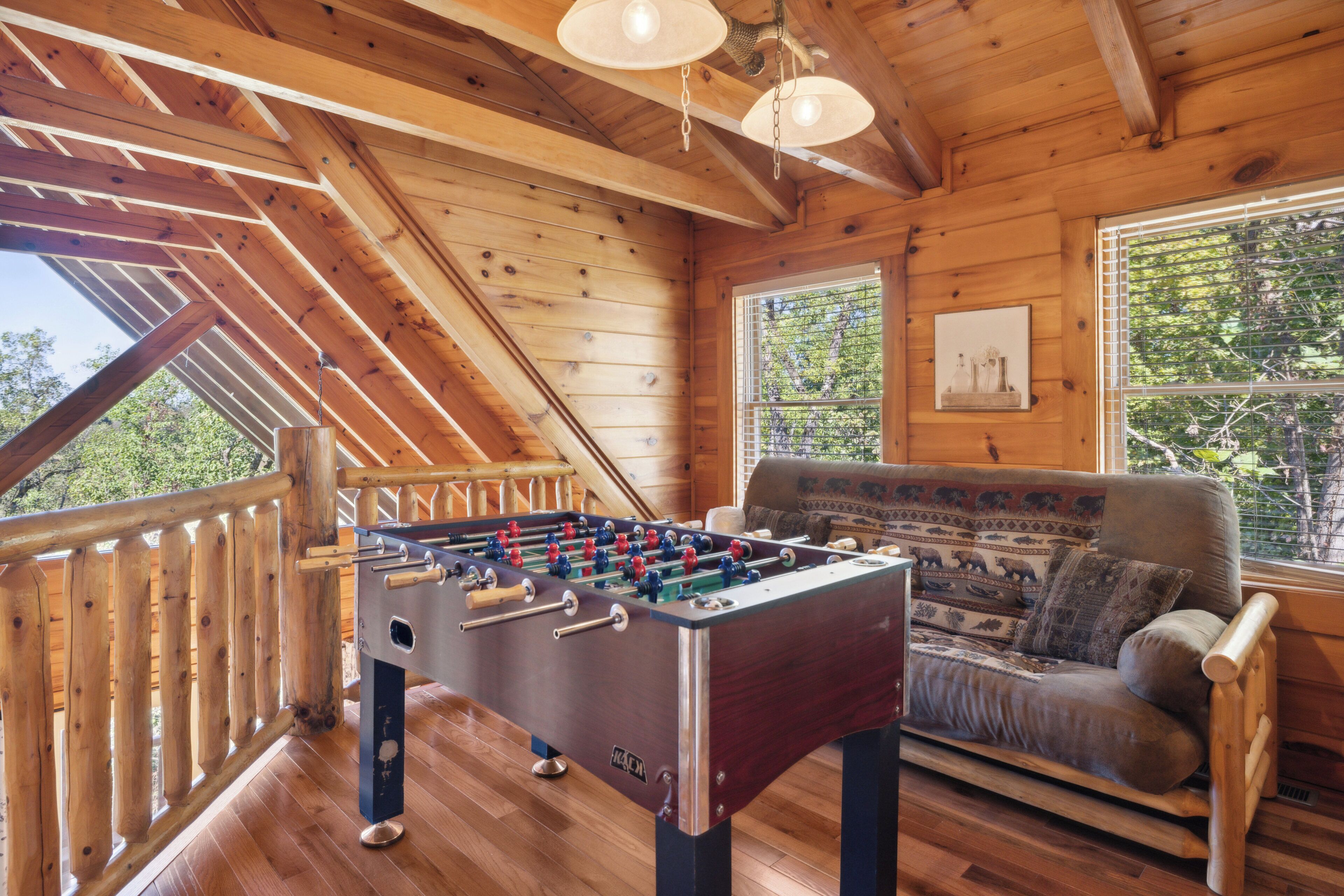 A wooden-floored room with a foosball table and a sofa.