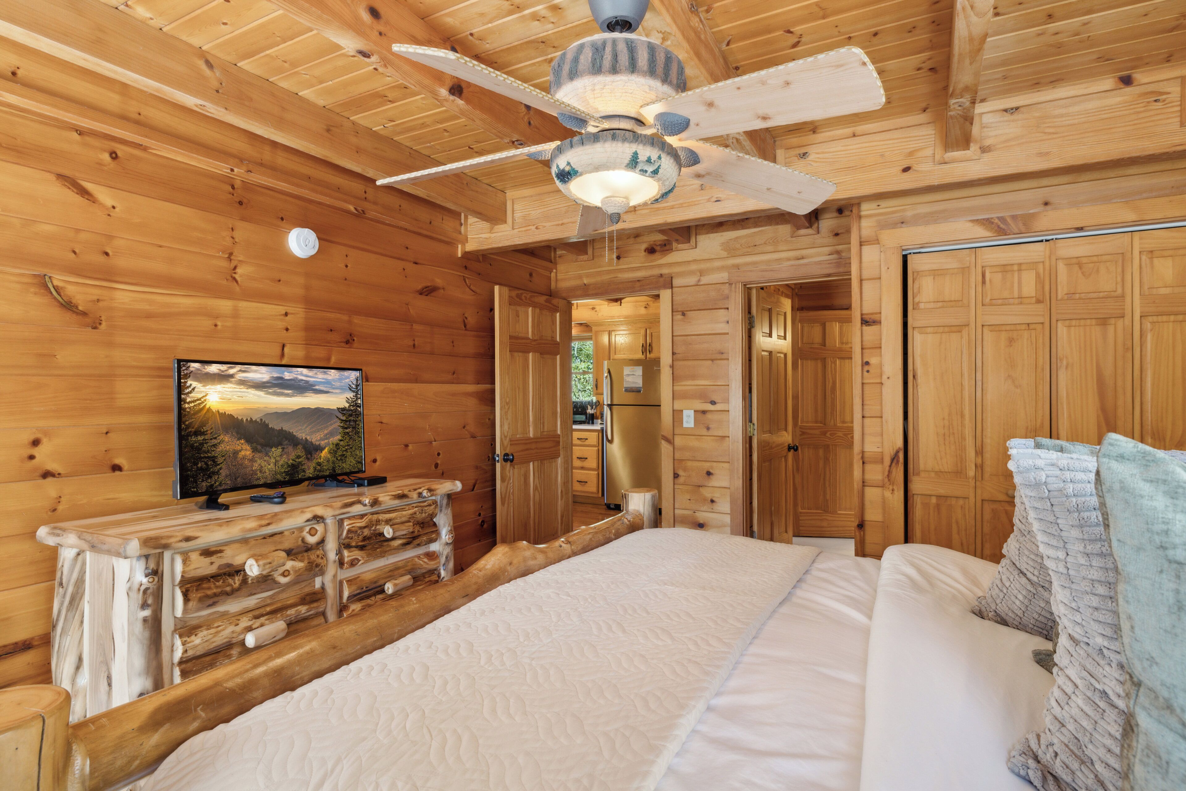Een slaapkamer in een houten blokhut, met een bed, een dressoir, een televisie en een plafondventilator.