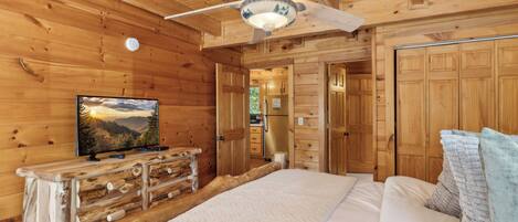 Een slaapkamer in een houten blokhut, met een bed, een dressoir, een televisie en een plafondventilator.