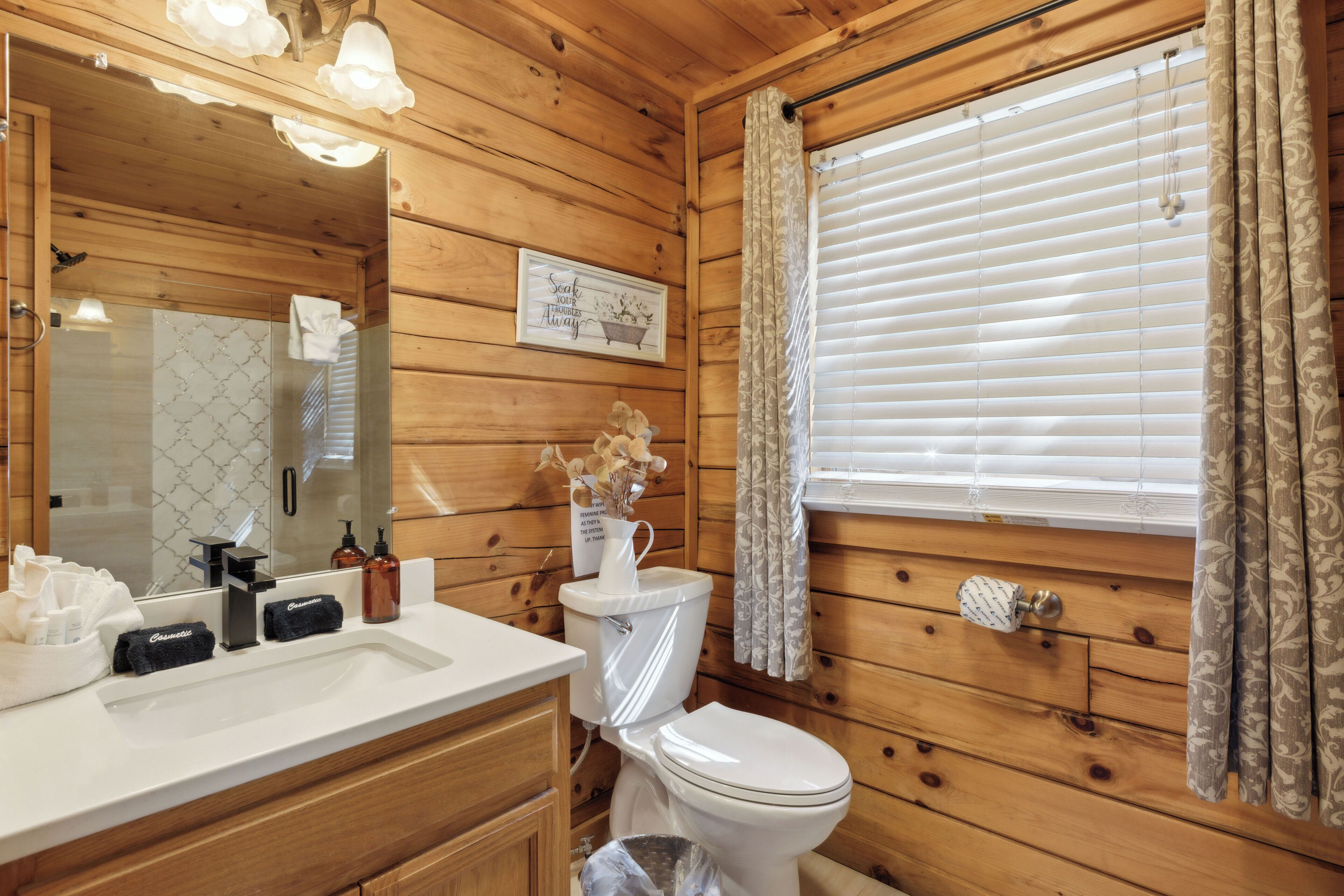 Un baño de cabaña de madera con un lavabo blanco, un inodoro y un espejo grande.