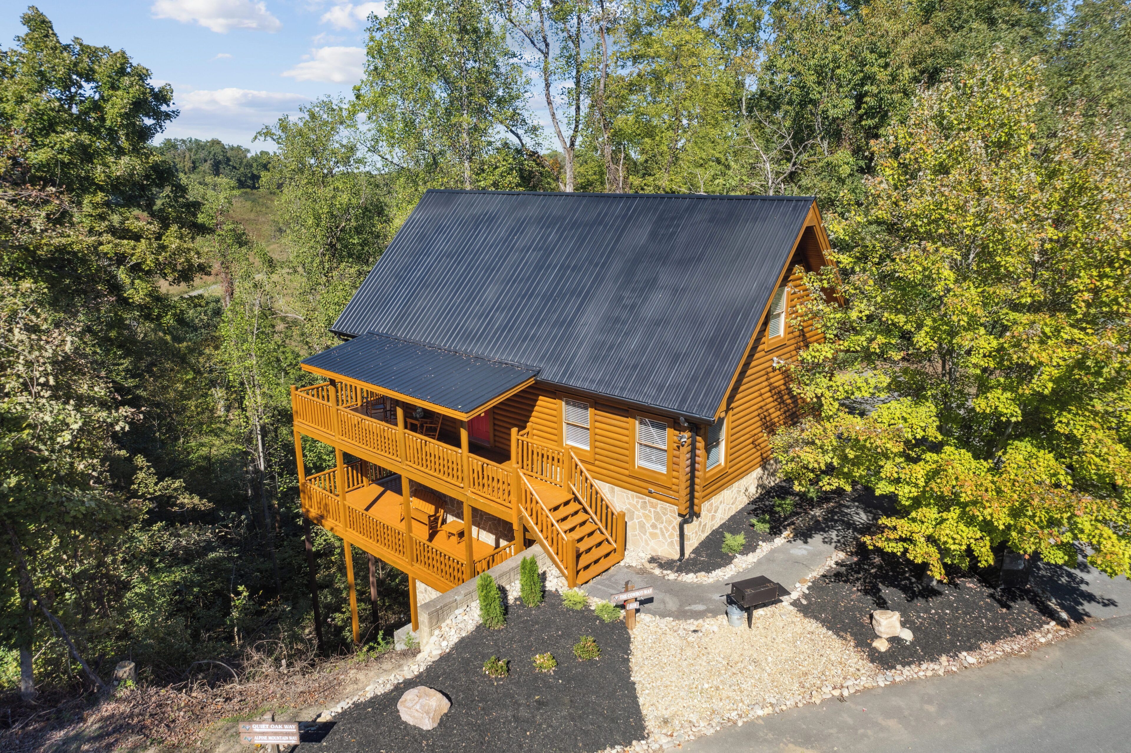 Una cabaña de madera con techo metálico, una terraza de madera y cimientos de piedra, rodeada de bosque.