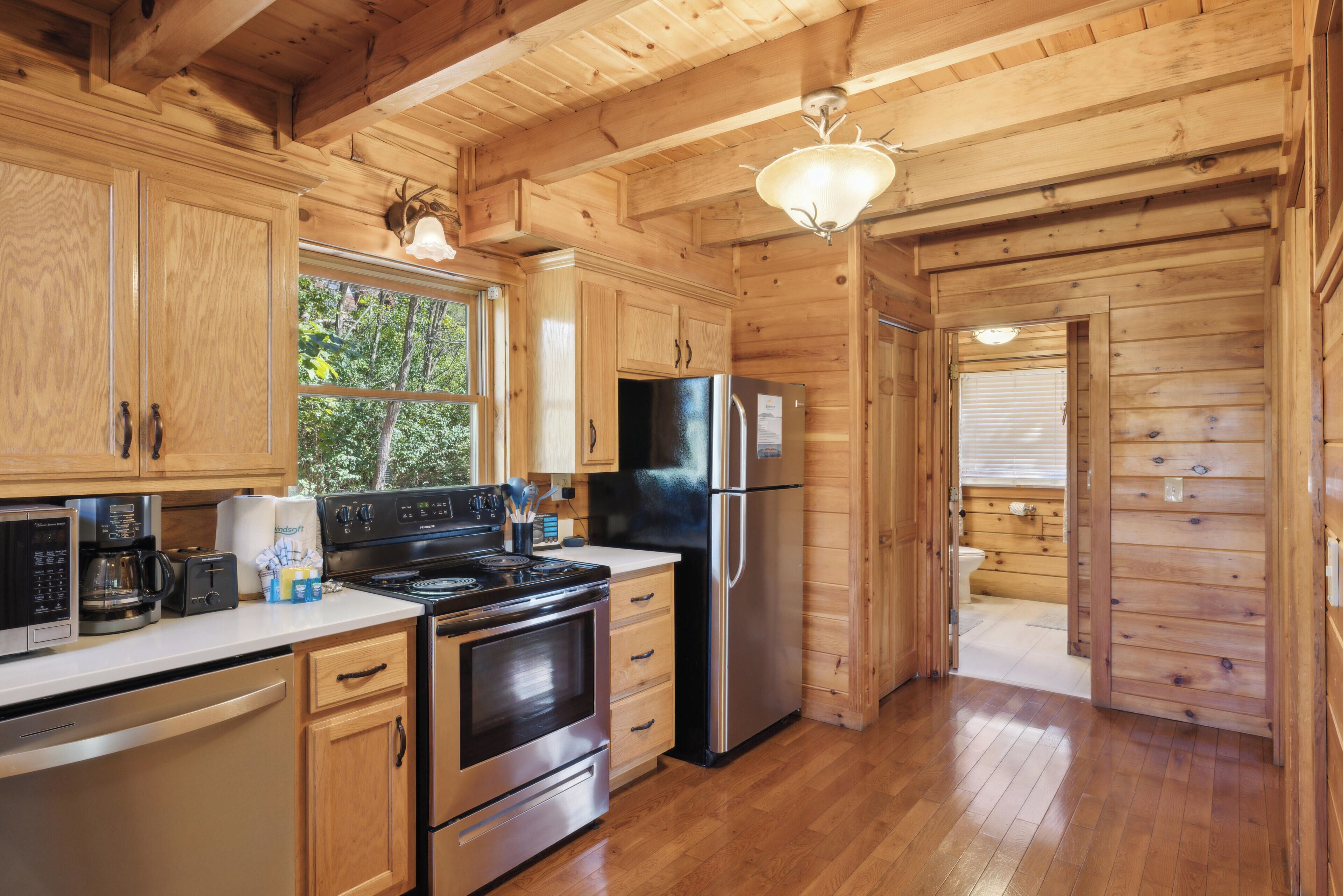 Une cuisine rustique, située dans une cabane en bois, équipée d’un poêle, d’un réfrigérateur et de meubles de rangement en bois.