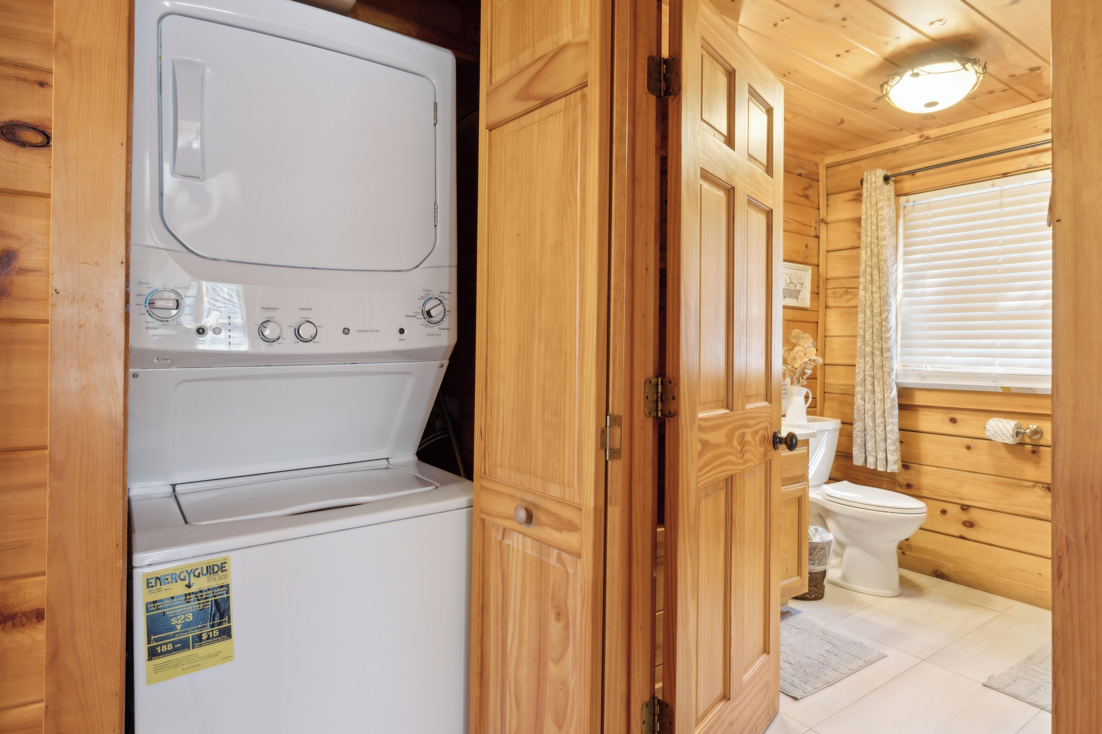 Une petite cabane en bois, équipée d’un lave-linge, de toilettes et d’une fenêtre avec des stores.