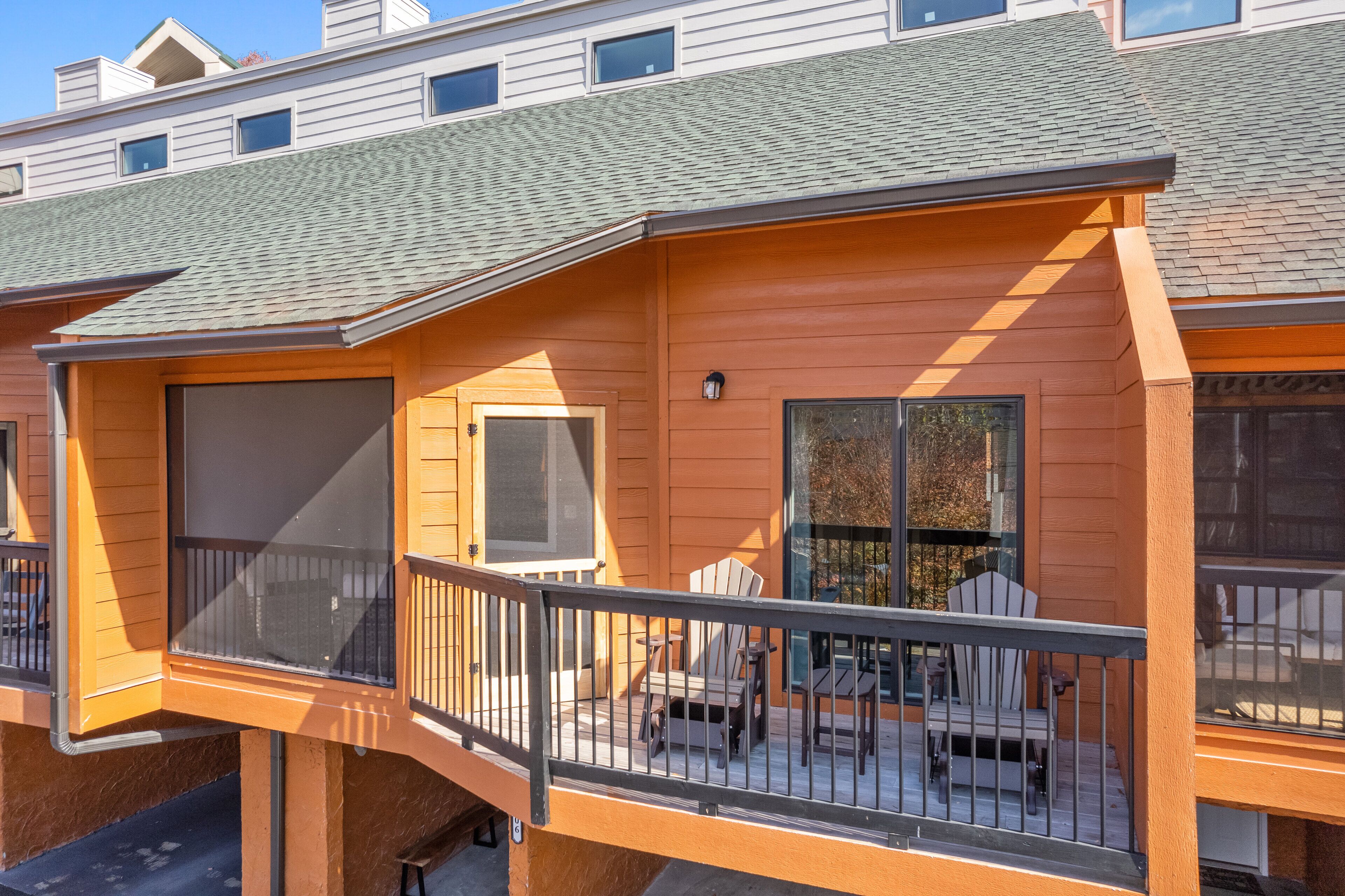 A wooden cabin with a balcony, a screened porch, and a table with chairs.