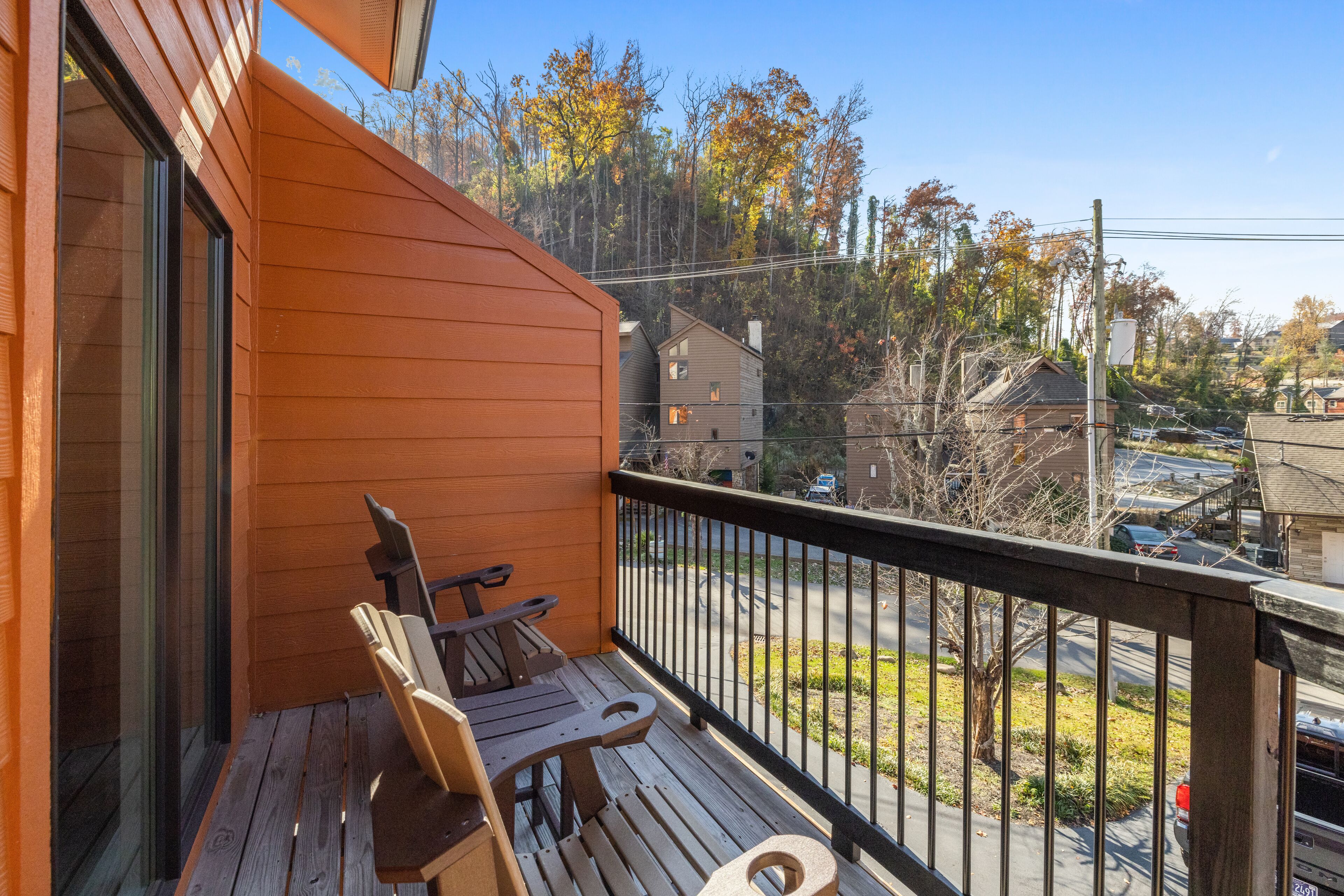 A wooden deck with two chairs and a table, overlooking a street with cars and houses.