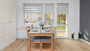 A dining area with a wooden table set for four, a window with blinds, and a view of the outside.