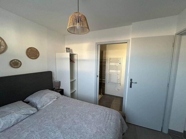 A bedroom with a bed, a wardrobe, a bedside table, and a hanging light fixture.