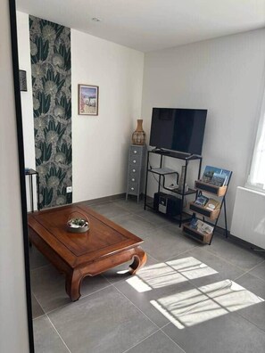 A modern living room with a wooden coffee table, a flat-screen TV on a stand, a small cabinet, and a bookshelf.