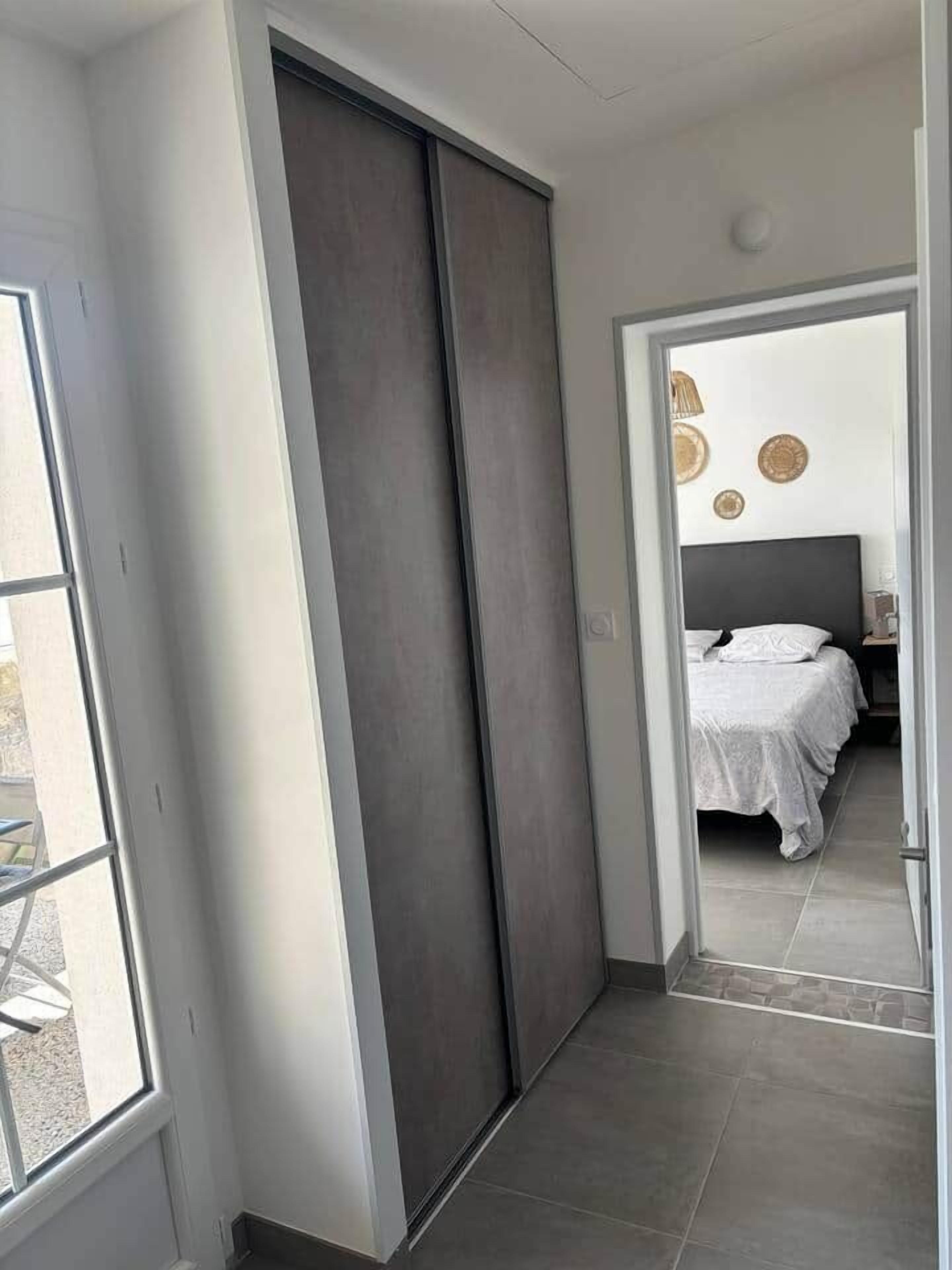 Un dormitorio moderno con una cama grande, una puerta corredera oscura y vistas al exterior a través de una ventana.