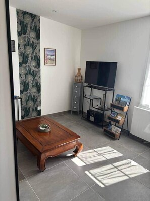 Ein modernes Wohnzimmer mit Couchtisch aus Holz, einem Flachbildfernseher auf einem Standfuß, einer kleinen Kommode und einem Bücherregal.