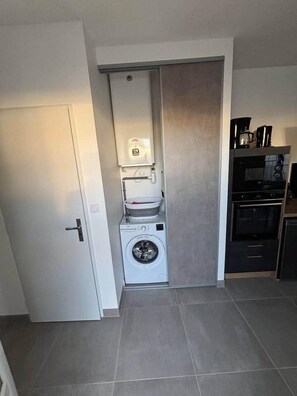 Eine kompakte Küche mit Waschmaschine, Kaffeemaschine und Mikrowelle.