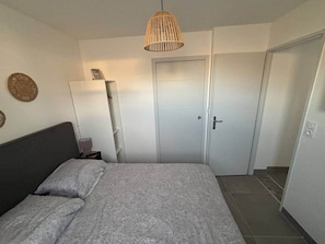Ein Schlafzimmer mit Bett, Nachttisch, Lampe, Kleiderschrank und einer Pendelleuchte.