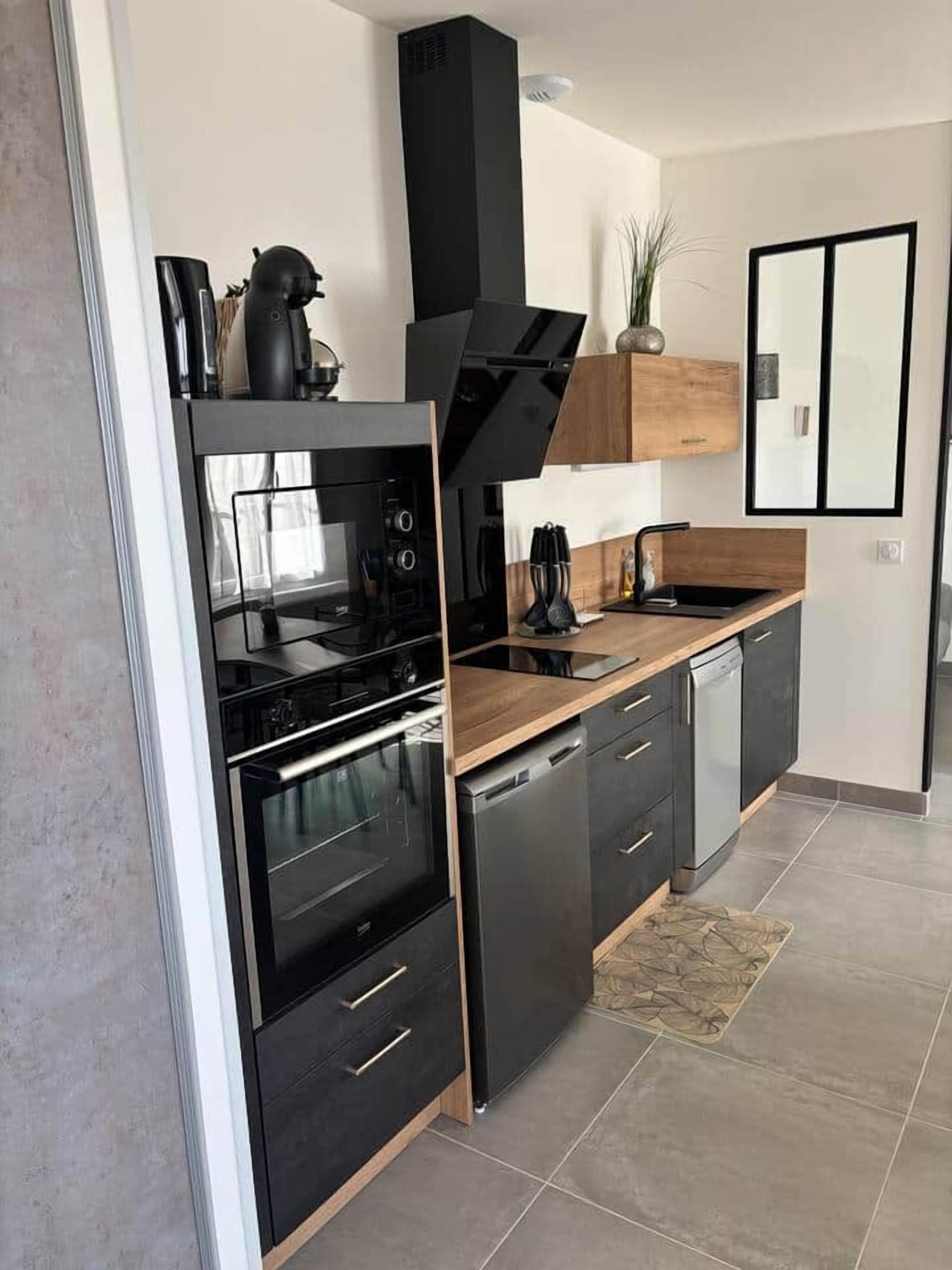 Une cuisine moderne avec des appareils électroménagers noirs, un plan de travail en bois et un four encastré.