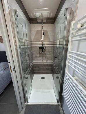A glass-enclosed shower with a handheld showerhead, a control panel above, and a towel rack on the right.