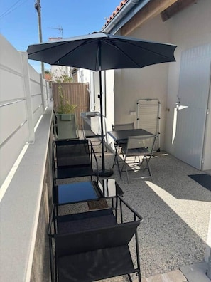 Eine Terrasse mit Tisch und Stühlen, einem schwarzen Sonnenschirm und einer weißen Garagentür.