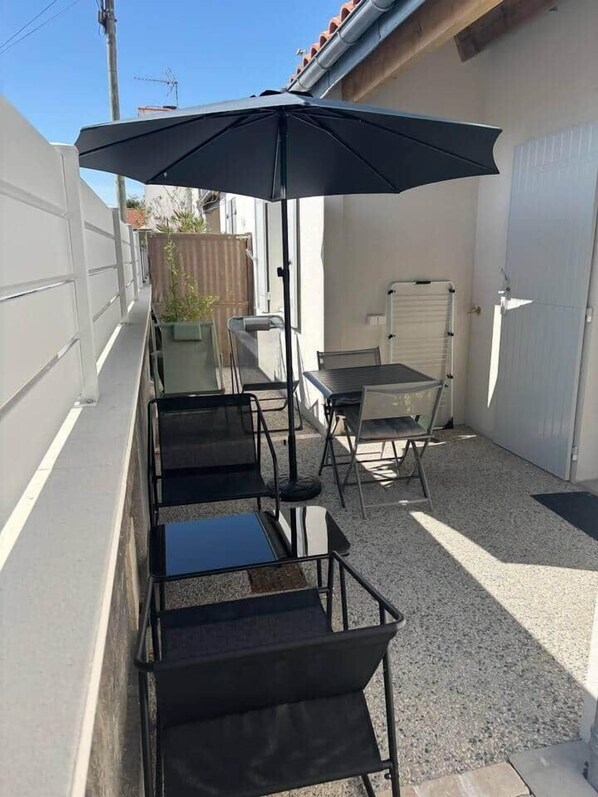 A patio with a table and chairs, a black umbrella, and a white garage door.