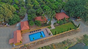 An aerial view of a resort with a swimming pool, multiple buildings with red roofs, and lush greenery surrounding the property. -  GIR LION SAFARI CAMP (Mendarda)