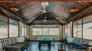A spacious indoor area with a pool table, foosball table, and seating along the walls. -  GIR LION SAFARI CAMP (Mendarda)