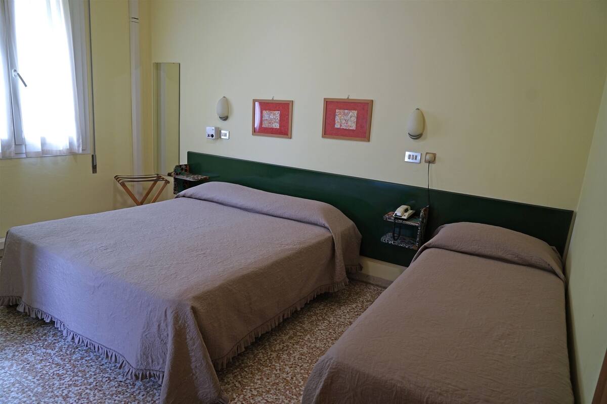 A hotel room with two beds, a small table, a chair, and a wall-mounted telephone.