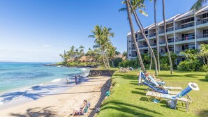 A beach with lounge chairs, palm trees, and a hotel in the background. - Upgraded beachside condo with ground floor access (Lahaina)
